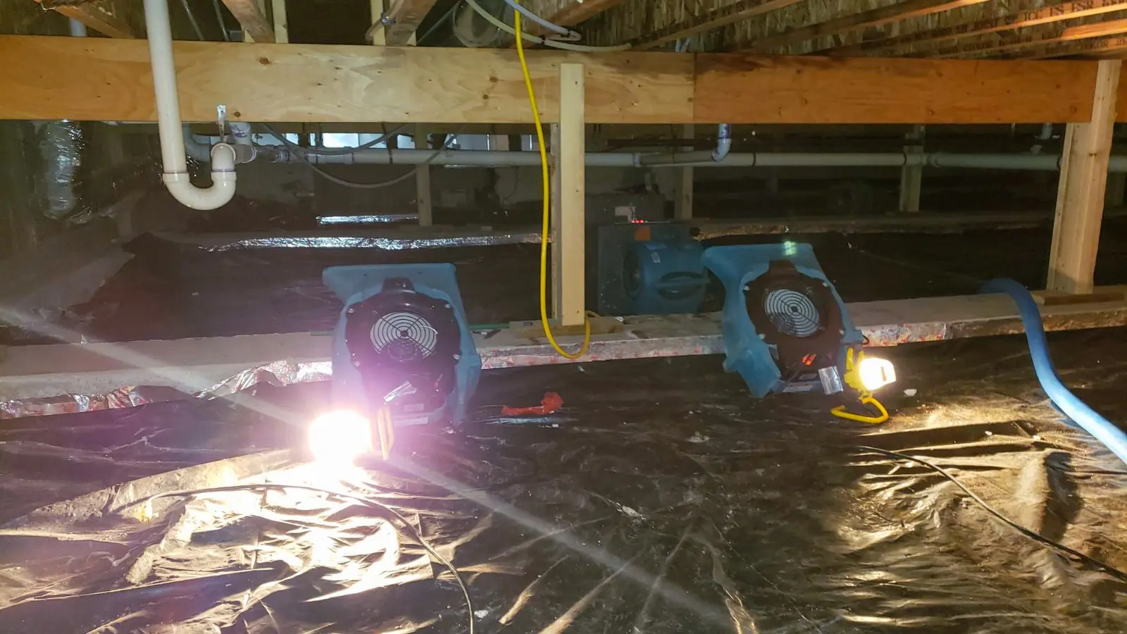 Air movers and work light drying a crawl space covered with plastic sheeting