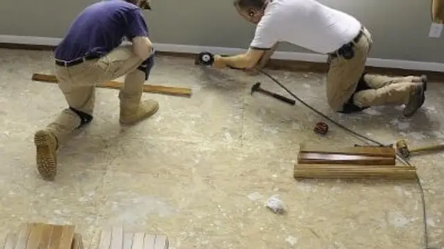 Two workers kneeling on a bare subfloor while preparing flooring repairs after water damage